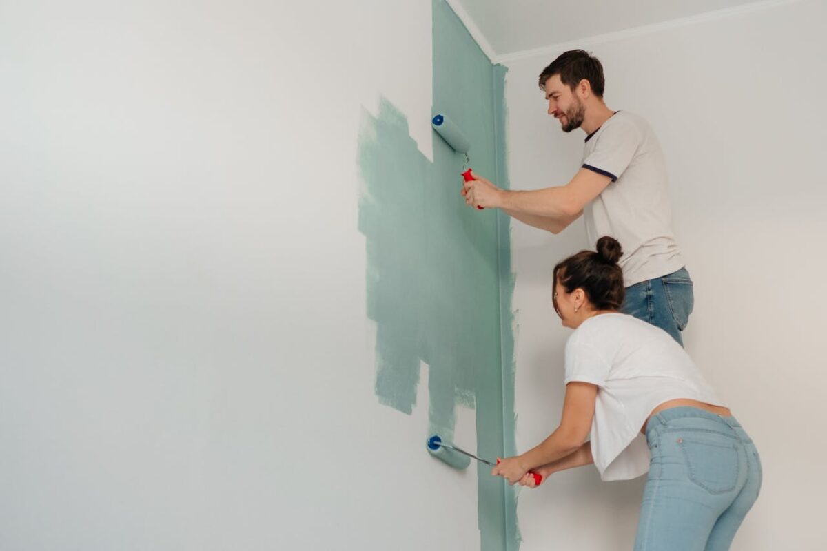 services-04 A young couple collaborates on painting a wall with rollers, highlighting teamwork and home improvement.