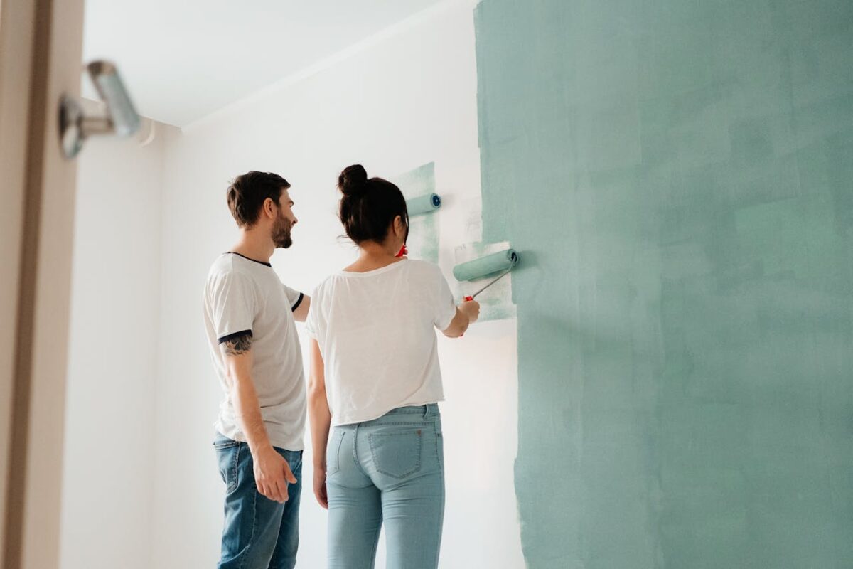 services-02 A couple collaborates to paint a wall with a roller indoors, showcasing teamwork.