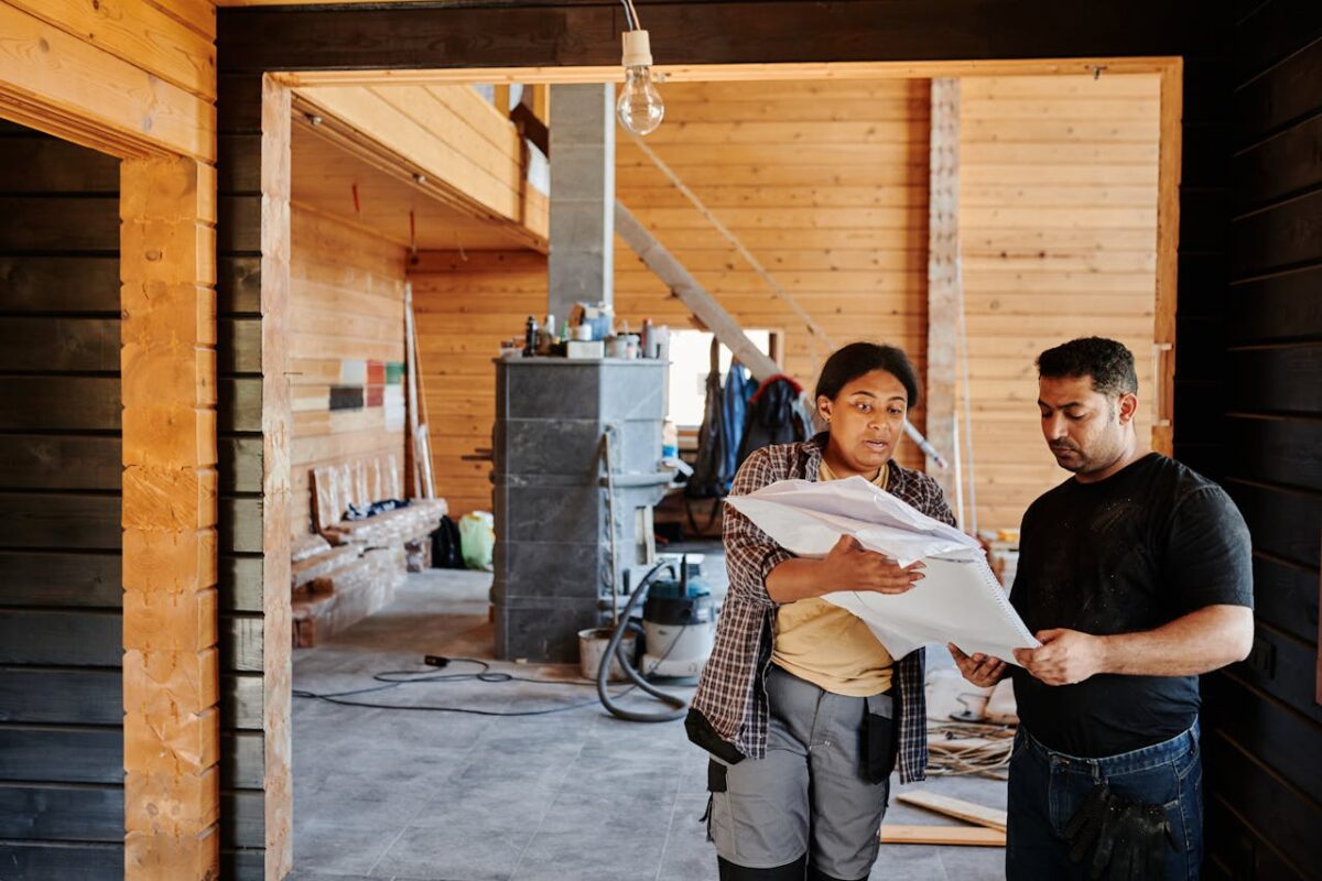 services-01 Construction workers reviewing blueprints indoors at a renovation site with wooden walls.